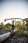 Hombre equilibrando cuidadosamente el árbol por encima de la cabeza mientras camina sobre el tronco - foto de stock