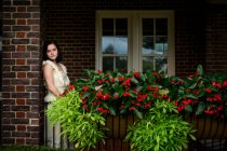 Beautiful young woman standing on a shadowed flower-filled porch — Stock Photo