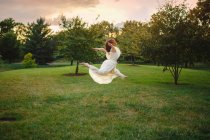 Tänzerin im langen weißen Kleid wirbelt bei Sonnenuntergang in goldenem Licht im Park — Stockfoto