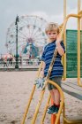 A little boy stands in front of a ferris wheel at Coney Island. — Stock Photo
