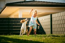 Baby girl running with beagle dog in backyard in summer day. Domestic animal with children concept. — Stock Photo