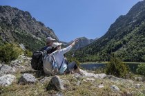Vue latérale du couple d'âge moyen assis sur la montagne des Pyrénées espagnoles et la femme pointe vers le sommet — Photo de stock