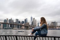 Привлекательная молодая женщина наблюдает за Бруклинским мостом из реки Гудзон в Нью-Йорке — стоковое фото