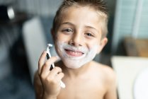 Маленький мальчик бреется как взрослый в ванной перед зеркалом — стоковое фото