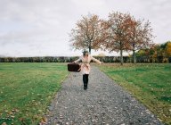 Frau geht mit offenen Armen und fühlt sich glücklich, einen Koffer zu tragen — Stockfoto