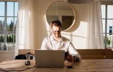 Mann arbeitet von zu Hause aus und blickt konzentriert auf Handy und Laptop — Stockfoto