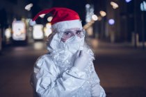 Портрет человека, одетого как Санта-Клаус, но со всеми предосторожностями против ковида 19, сфотографированный во время ношения маски для лица. — стоковое фото