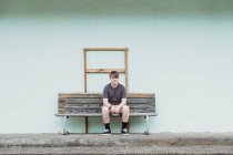 Teenage boy sitting alone on a wooden bench seat — Stock Photo