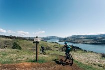 Two young girls bike along a trail overlooking the Columbia River. — Stock Photo