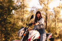 Mulher jovem confiante andando de moto em meio a árvores na floresta — Fotografia de Stock