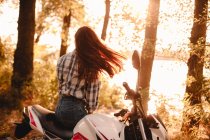 Jeune femme jetant les cheveux tout en se relaxant assis sur la moto par la rivière — Photo de stock