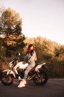 Молодая женщина оглядывается назад, сидя на мотоцикле по проселочной дороге в лесу — стоковое фото