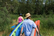 Una joven pareja lleva tablas de remo al agua en Oregon. - foto de stock