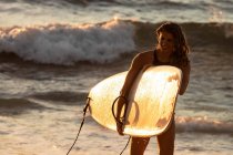 Une surfeuse quitte l'océan avec une planche de surf au coucher du soleil à Hawaï — Photo de stock