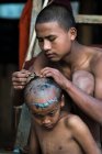Молодой монах бреет волосы на голове послушника с бритвой, недалеко от Сипау, Мьянма — стоковое фото