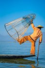 Вид сзади на Интху рыбак позирует с типичной конической рыболовной сетью на лодке против ясного голубого неба, озера Инле, Ньянгшве, Мьянма — стоковое фото