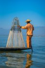 Vista posteriore di Intha pescatore in piedi con tipica rete da pesca conica in barca contro il cielo blu chiaro, Lago Inle, Nyaungshwe, Myanmar — Foto stock