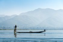 Рыбак с помощью рыболовной сети на лодке против гор, озера Инле, Ньянгшве, Мьянма — стоковое фото