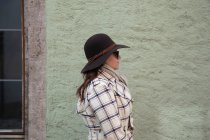 Женщина в шляпе и солнечных очках, стоящая одна у каменной стены — стоковое фото
