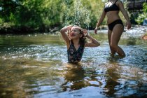 Heureuse jeune fille éclaboussant dans un ruisseau par une journée chaude — Photo de stock
