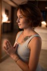 Vista lateral de la mujer cogiéndose de las manos y meditando mientras practica yoga por la noche - foto de stock