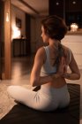 Rückenansicht einer jungen Frau, die in Lotus-Pose sitzt und mit gefalteten Händen meditiert — Stockfoto