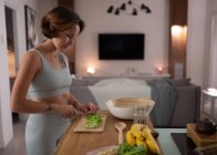 Junge Frau hackt frischen Salat, während sie vegetarischen Salat zum Abendessen kocht — Stockfoto