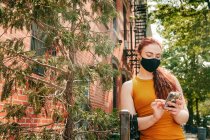 Junge Frau am Telefon trägt Gesichtsmaske in der Straße von Brooklyn an Bäumen — Stockfoto