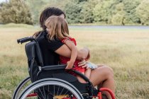 Mãe deficiente em uma cadeira de rodas abraçando sua filhinha com um gre — Fotografia de Stock