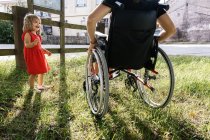 Маленька дівчинка посміхається поруч з матір'ю в інвалідному візку в зеленому віолончелі — стокове фото