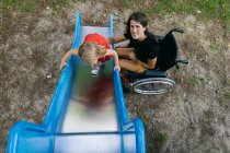 Улыбающаяся мать в инвалидном кресле играет со своей маленькой дочкой на s — стоковое фото