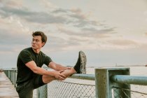 Männlicher Athlet dehnt sich bei Sonnenuntergang am Wasser — Stockfoto