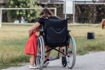 Мать в инвалидном кресле обнимает свою маленькую дочь зеленым полем — стоковое фото