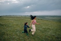 Mom and daughter running down hill in countryside — Stock Photo