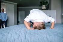 Молодий хлопчик грає на батьківському ліжку, поки тато дивиться — стокове фото