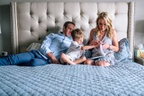 Family relaxing and reading a book on a bed in the afternoon — Stock Photo