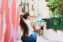 A young woman with sunglasses and a backward glance sits on a staircase in the middle of an alley painted pink and red. Concept of tourism — Stock Photo