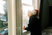 Little boy looking into window, happy child in winter — Stock Photo