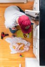 Blick von oben auf Vater repariert Küchenspüle, während Baby Mädchen zu Hause auf Hartholzboden liegt — Stockfoto