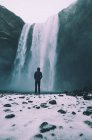 Человек, стоящий у водопада Скогафосс зимой со снегом на переднем плане — стоковое фото