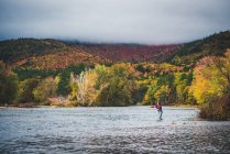 Woman angler casting into river with clouds and bright foliage — Stock Photo