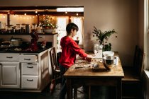 Bambino che fa biscotti nella sua cucina, con albero di Natale sullo sfondo — Foto stock