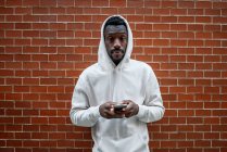 Front shot of African man with serious gesture and hood using smartphone in city — Foto stock