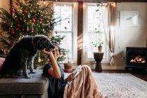 Happy young woman reading while petting her dog, by fireplace — Stock Photo