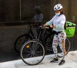 Девушка с велосипедом и зеленой коробкой перед черной стеной и смотрит — стоковое фото