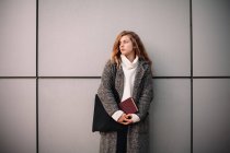 Ritratto di studentessa premurosa che tiene il libro in piedi contro il muro grigio — Foto stock