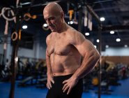 Сильный старший спортсмен с руками на талии делает паузу в интенсивной функциональной тренировке в современном тренажерном зале — стоковое фото