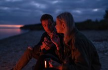 Vue latérale d'un jeune couple fumant un joint de marijuana assis dans la nature lors d'une nuit d'automne nuageuse — Photo de stock