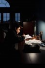 Adolescent garçon dessin à un bureau dans un sombre chambre par lampe lumière. — Photo de stock