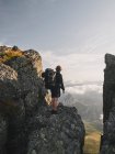 Молодой мужчина с рюкзаком стоит на скале и смотрит на пейзаж — стоковое фото
